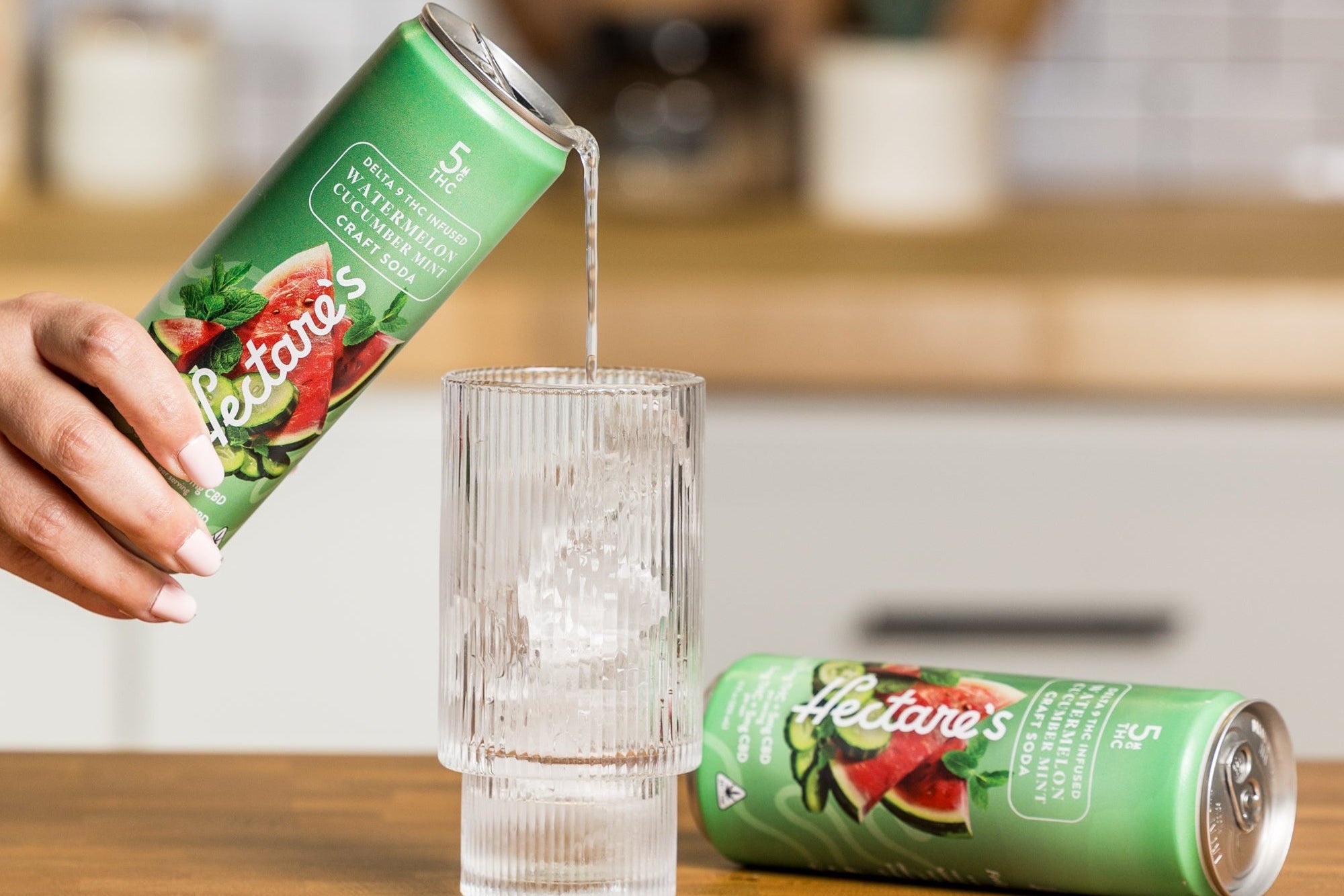 Person pouring a Hectare's Watermelon Cucumber Mint Delta 9 Craft Soda into a glass on a kitchen counter.