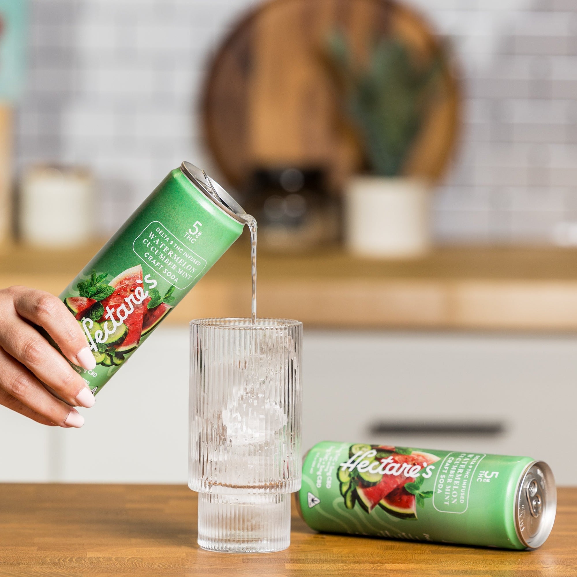 Person pouring a Hectare's Watermelon Cucumber Mint Delta 9 Craft Soda into a glass on a kitchen counter. 